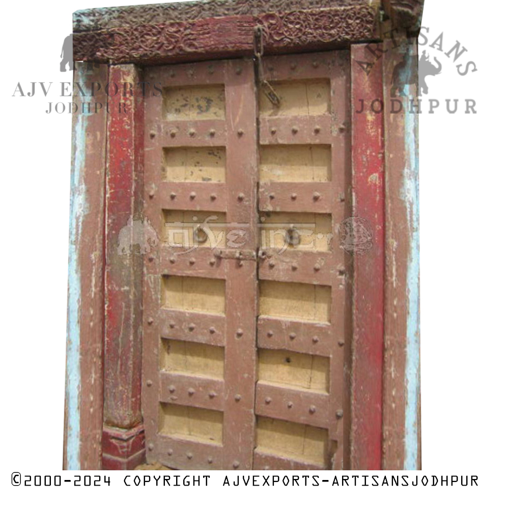 Weathered wooden door with faded red and blue paint, carvings, and metal studs