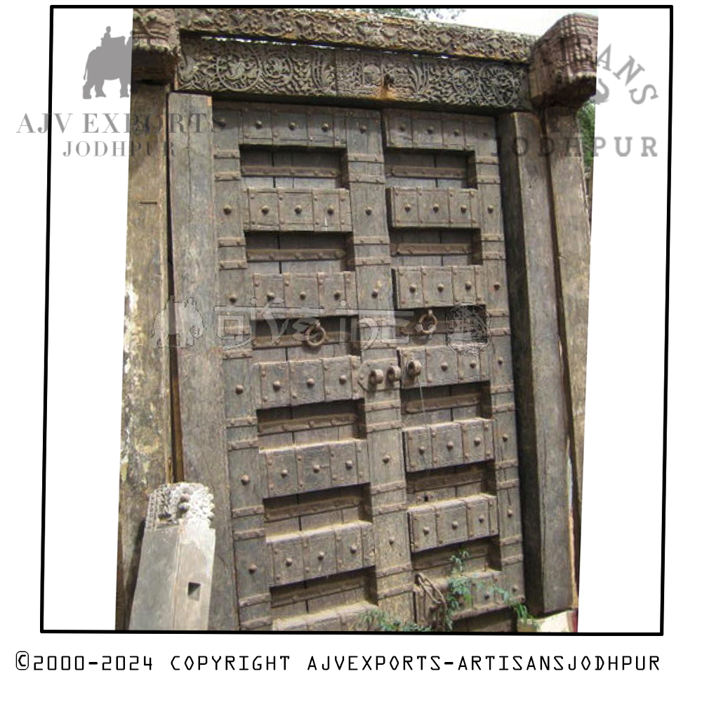 Ancient wooden door with elaborate carvings and metal studs, severely weathered