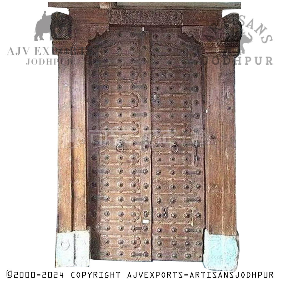 Old wooden door covered in metal studs with intricately carved frame