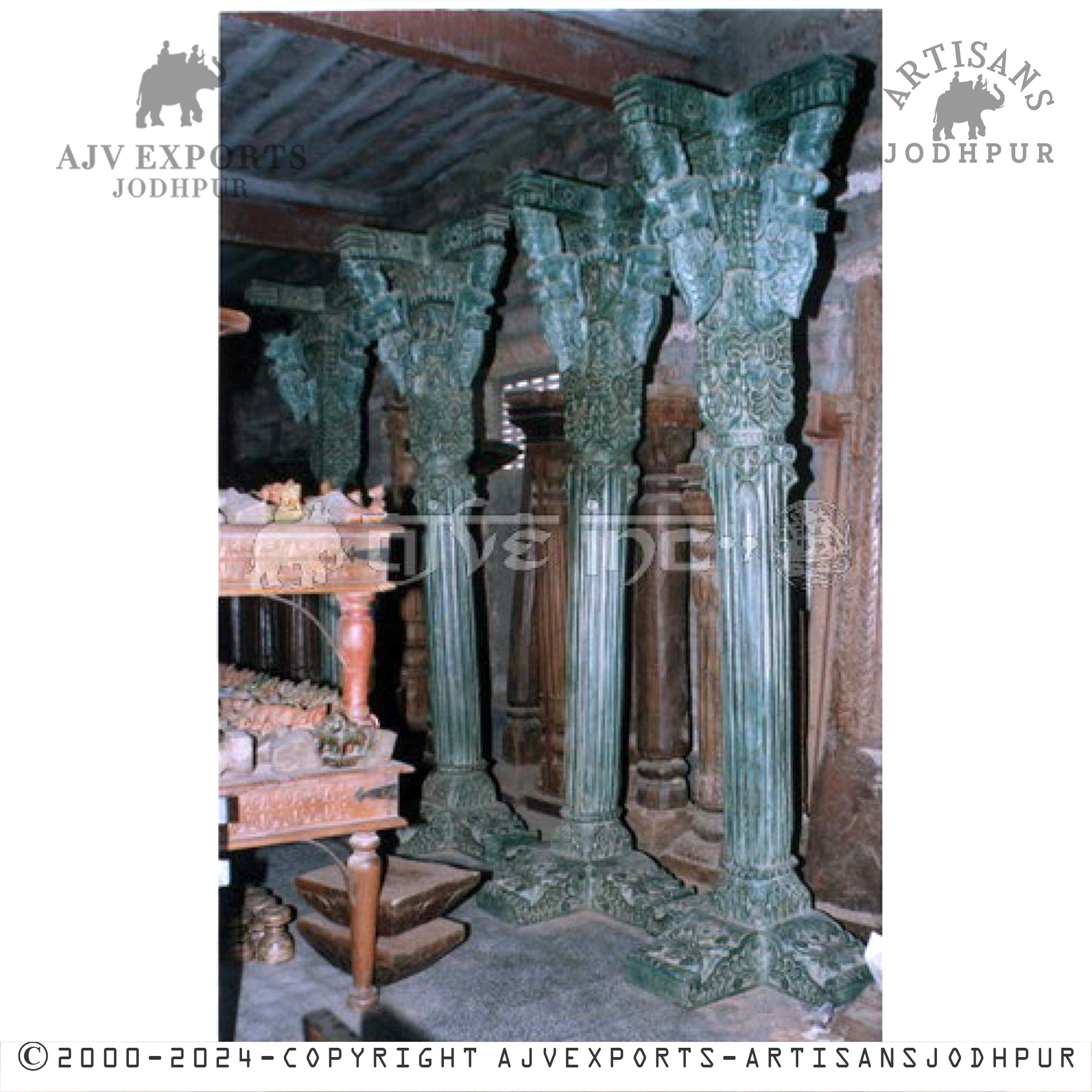 A group of teal-colored wooden columns with intricate carvings and detailed capitals, standing in a storeroom.