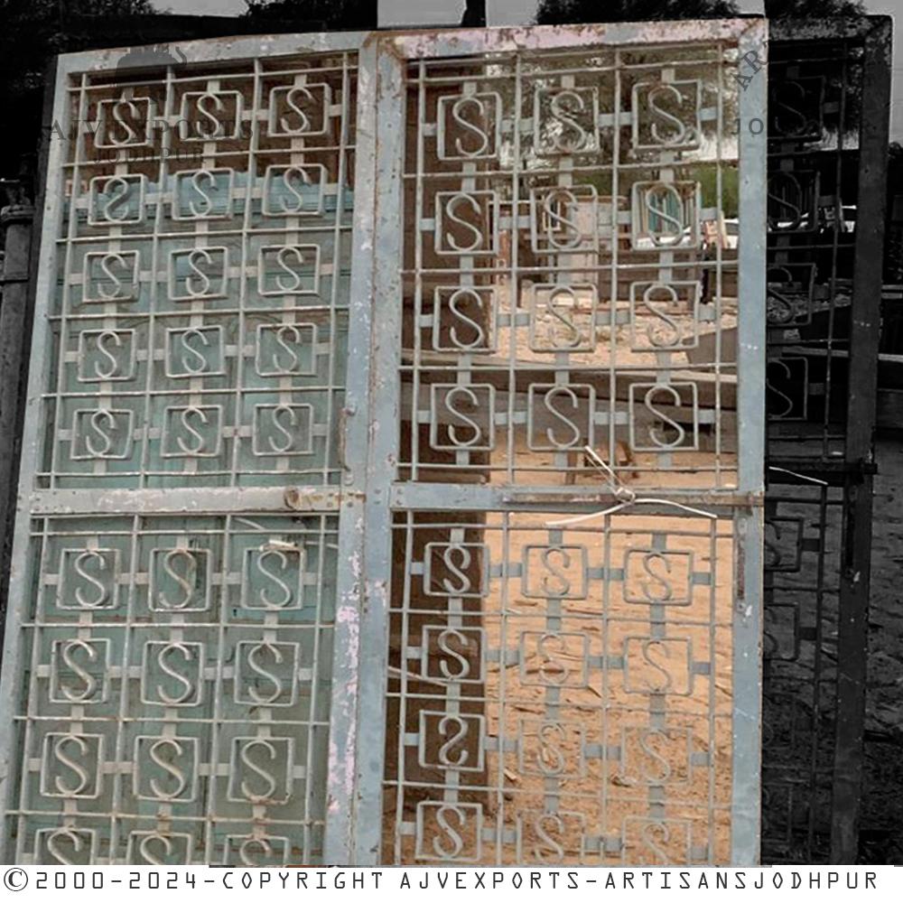 A pair of antique iron grill doors with a geometric pattern and stylized "S" shapes, showcasing a weathered patina.
