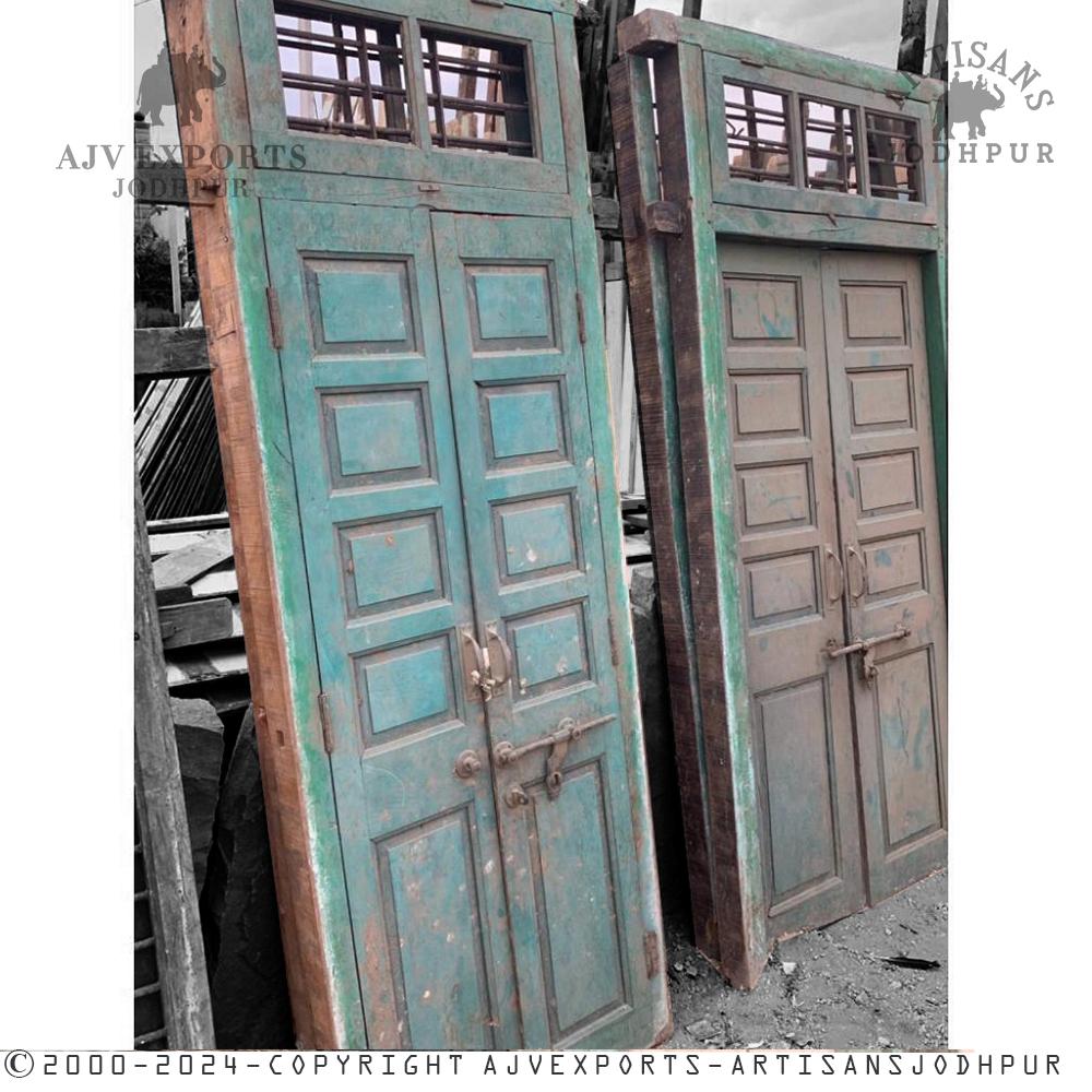A set of antique wooden doors with original green paint and wooden panel featuring metal hardware.